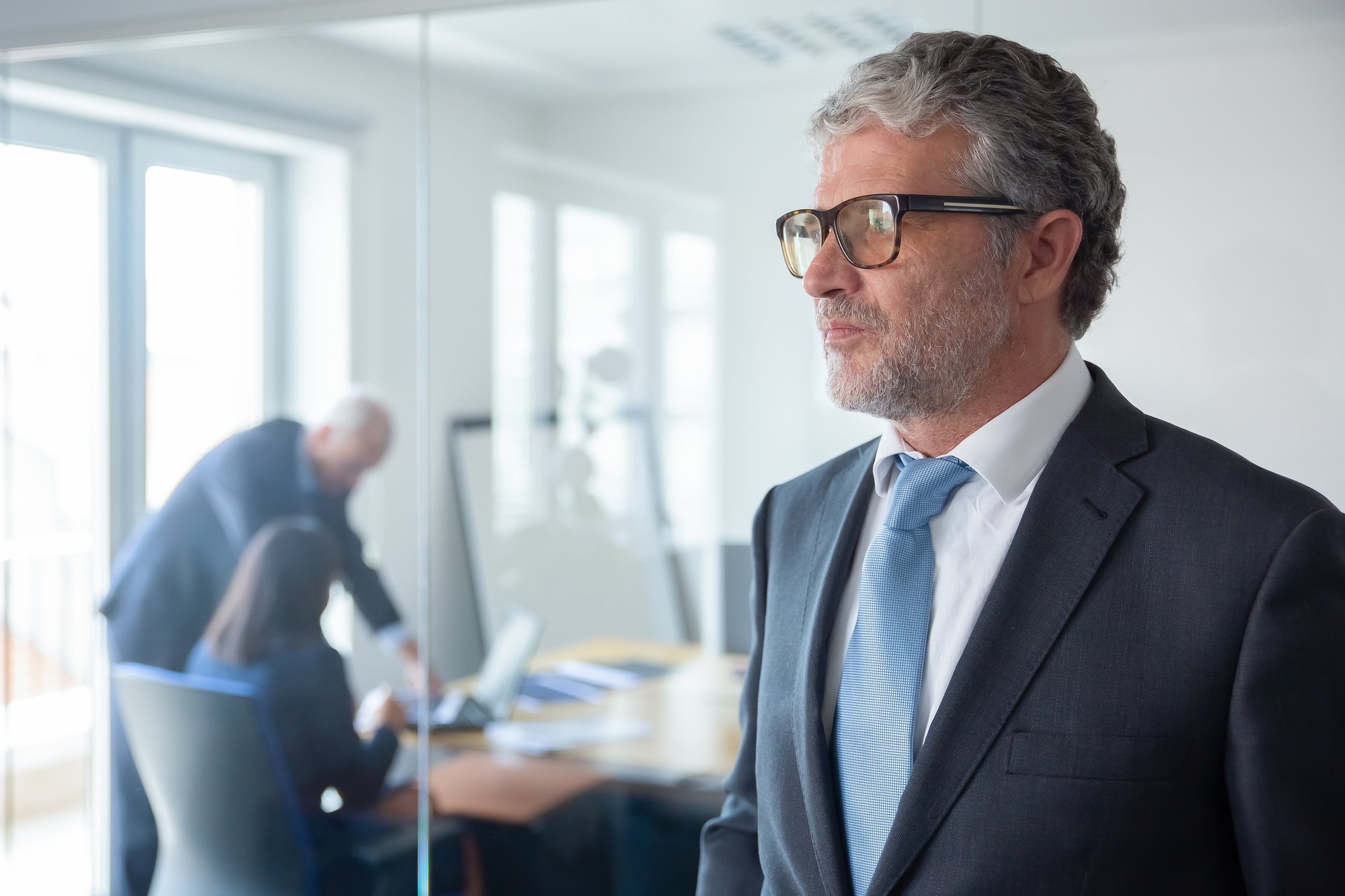 pensive-mature-businessman-formal-suit-glasses-standing-by-office-glass-wall-looking-away-copy-space-business-portrait-concept